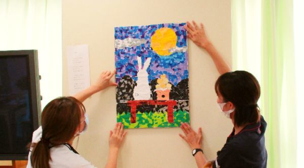 リハビリ職員と看護師が患者様と作成した作品を飾る風景